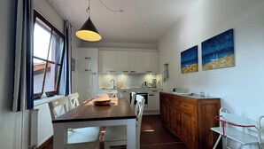 A modern kitchen with white cabinets, a wooden dining table, and a red-framed window. - Experience Frisian coziness in Haus Siril and the Kombüse apartment on Wangerooge (Wangerooge)