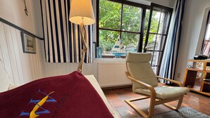 A room with a bed, a chair, a lamp, a window with a view of greenery, and a striped wall. - Experience Frisian coziness in Haus Siril and the Kombüse apartment on Wangerooge (Wangerooge)