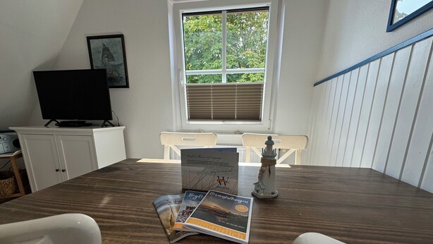 A dining area with a wooden table, two white chairs, a small decorative item, and a framed picture on the wall. - Oberdeck - Friesische Gemütlichkeit (Wangerooge)