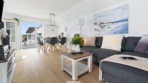 A modern living room with a sofa, coffee table, and a painting of a snowy landscape. - Ocean Time - 1st Floor, 2 Balconies, Infrared Sauna, Fireplace, Sun Loungers (Olpenitz)