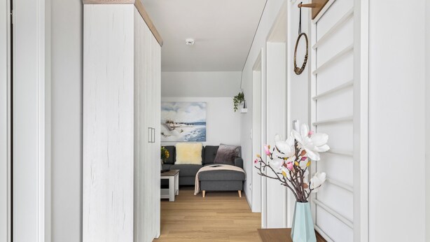 A hallway with a wooden floor, white walls, a grey sofa, and a vase with flowers. - Ocean Time - 1st Floor, 2 Balconies, Infrared Sauna, Fireplace, Sun Loungers (Olpenitz)