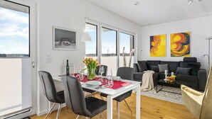 A modern living room with a dining area, large windows, and abstract wall art. - Ocean View 14 - Balcony, Grill, Fireplace, Shower, Elevator, Underground Parking (Olpenitz)