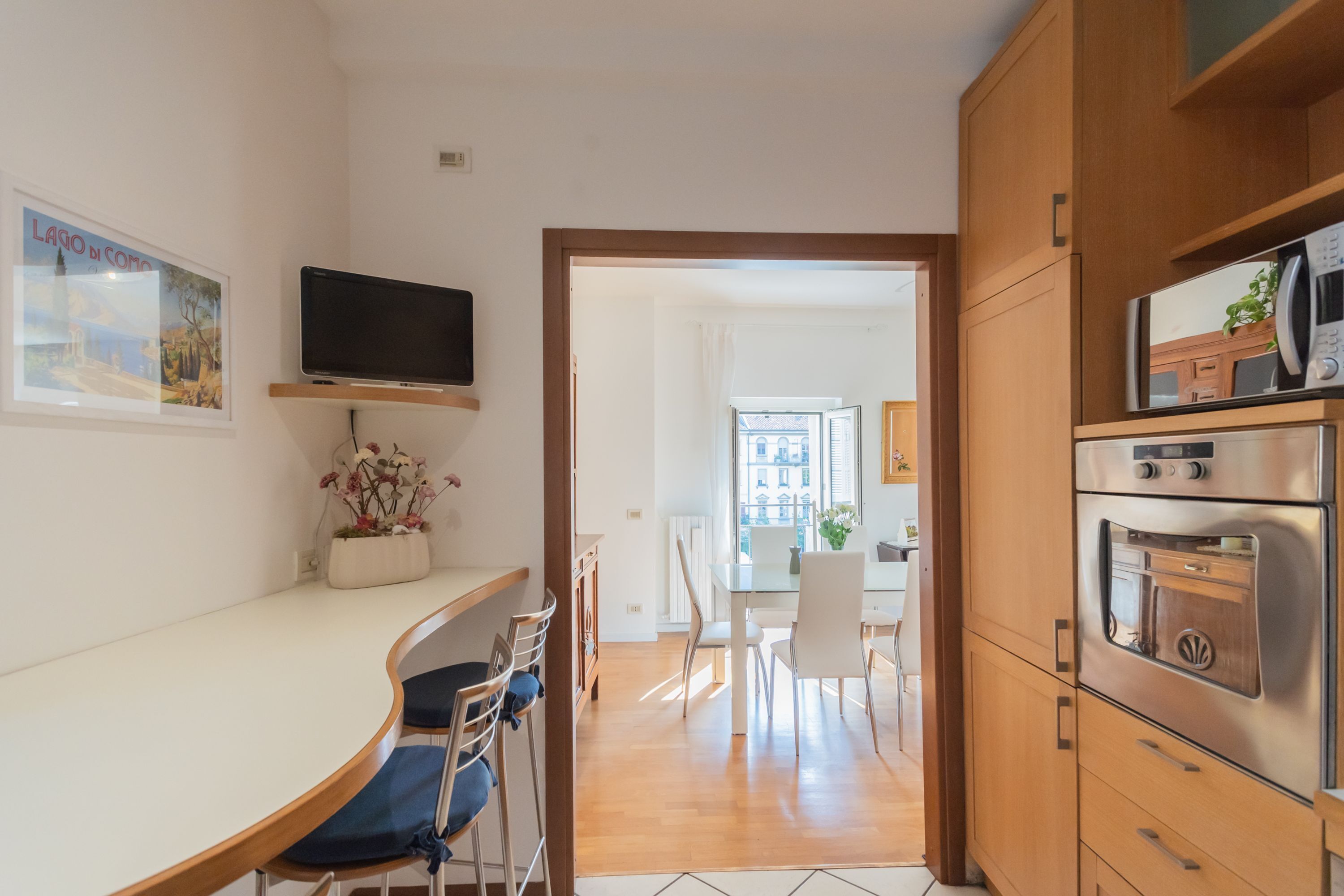 A modern kitchen with wooden cabinets, a built-in oven, and a TV mounted above the counter.