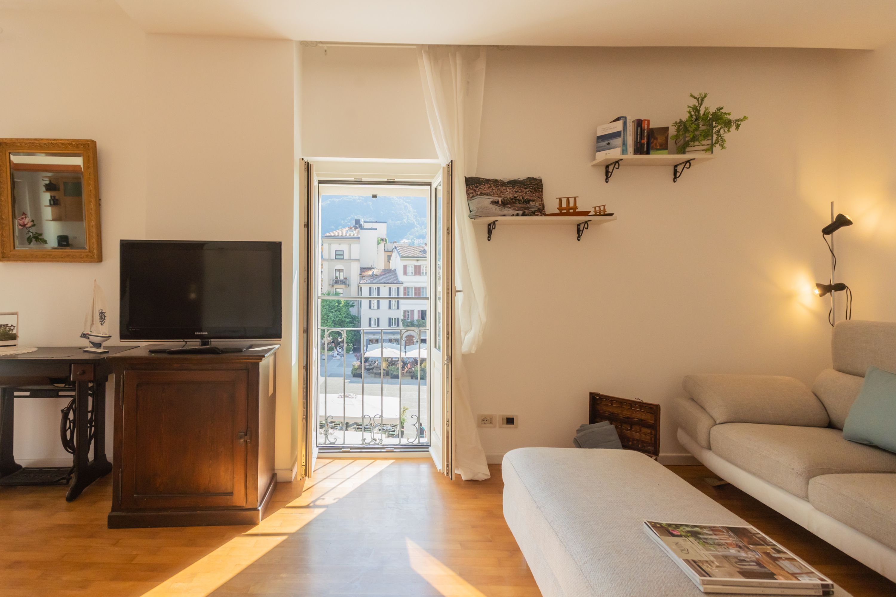 A living room with a television, a sofa, a bookshelf, and a view of buildings through a door.