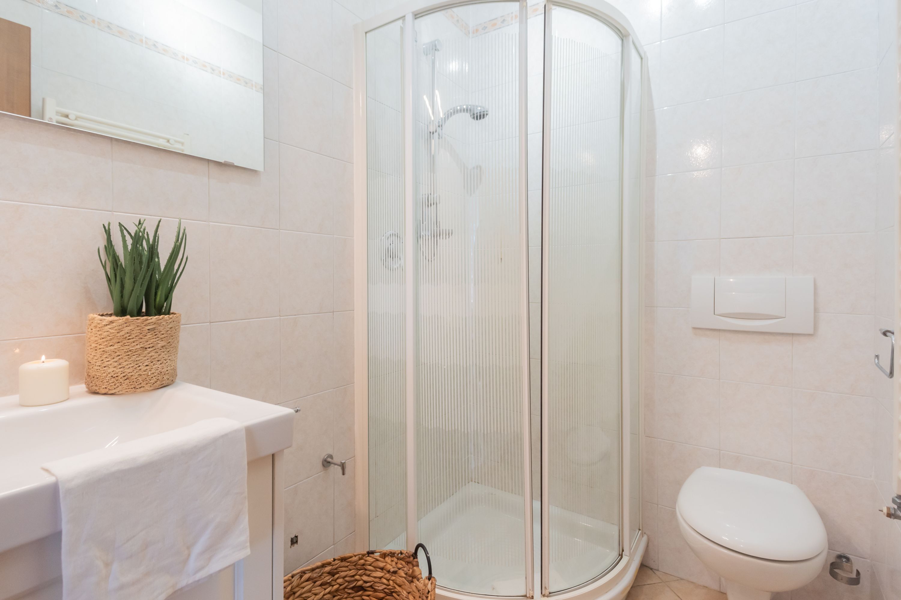 Een moderne badkamer met een douchecabine van glas, een toilet en een wastafel met een handdoek en een kaars.