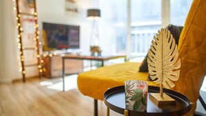 Un salon avec un canapé jaune, une table basse ornée d’un motif en forme de feuille et un téléviseur en arrière-plan.