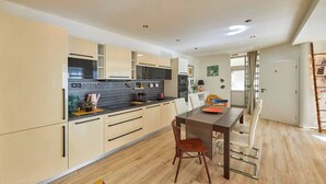 Une cuisine moderne avec des meubles de couleur claire, un plan de travail foncé et un coin repas comprenant une table et des chaises.