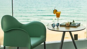 A room with a view of the ocean, a green chair, a table with a drink, sunglasses, and books. - The Sea View Cam Ranh (Bac Cam Ranh)