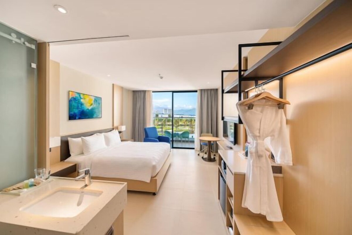 Ett modernt hotellrum med en stor säng, ett badrum med handfat och spegel, en badrock som hänger på en krok och utsikt över omgivningarna.