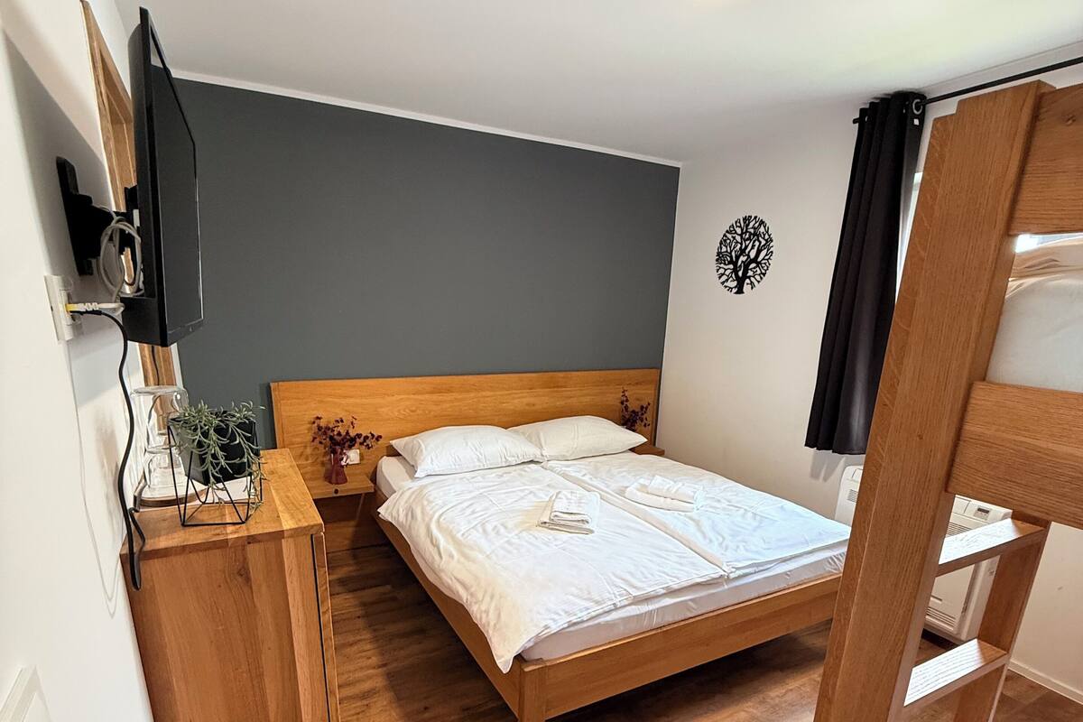 A small, cozy room with a single bed, a wooden nightstand, a TV mounted on the wall, and a ceiling light.