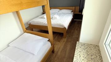 Ein Zimmer mit zwei Etagenbetten, Holzboden und einem Fenster mit Blick nach draußen.