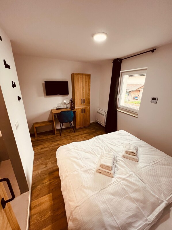 A bedroom with a bed, a desk, a chair, a wardrobe, a TV, and a window.