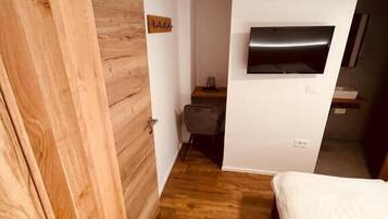 A bedroom with a wooden wardrobe, a bed, a TV mounted on the wall, and a small desk with a chair.