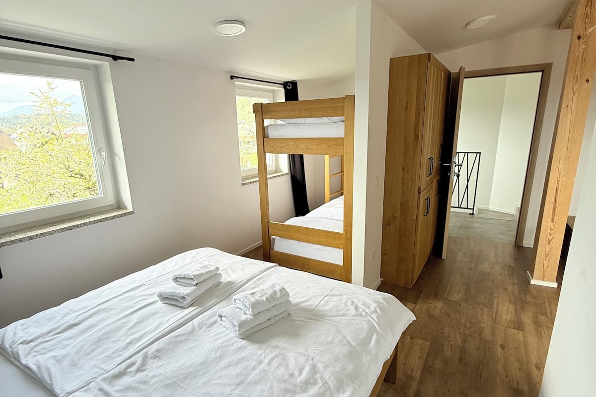 A bedroom with a bunk bed, a window with a view, and a wooden wardrobe.