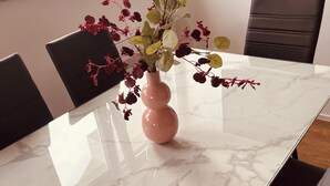 A marble table with a pink vase of flowers, black chairs, and a window with a view of buildings.
