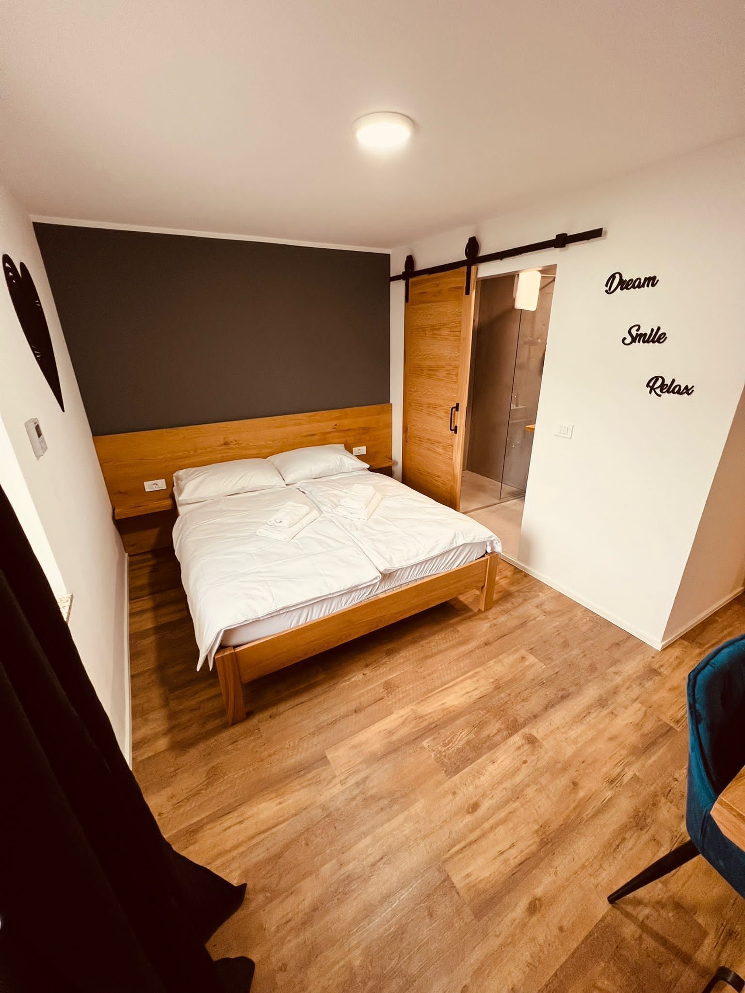 A modern bedroom with a wooden bed, a dark wall, and a wardrobe with a sliding door.