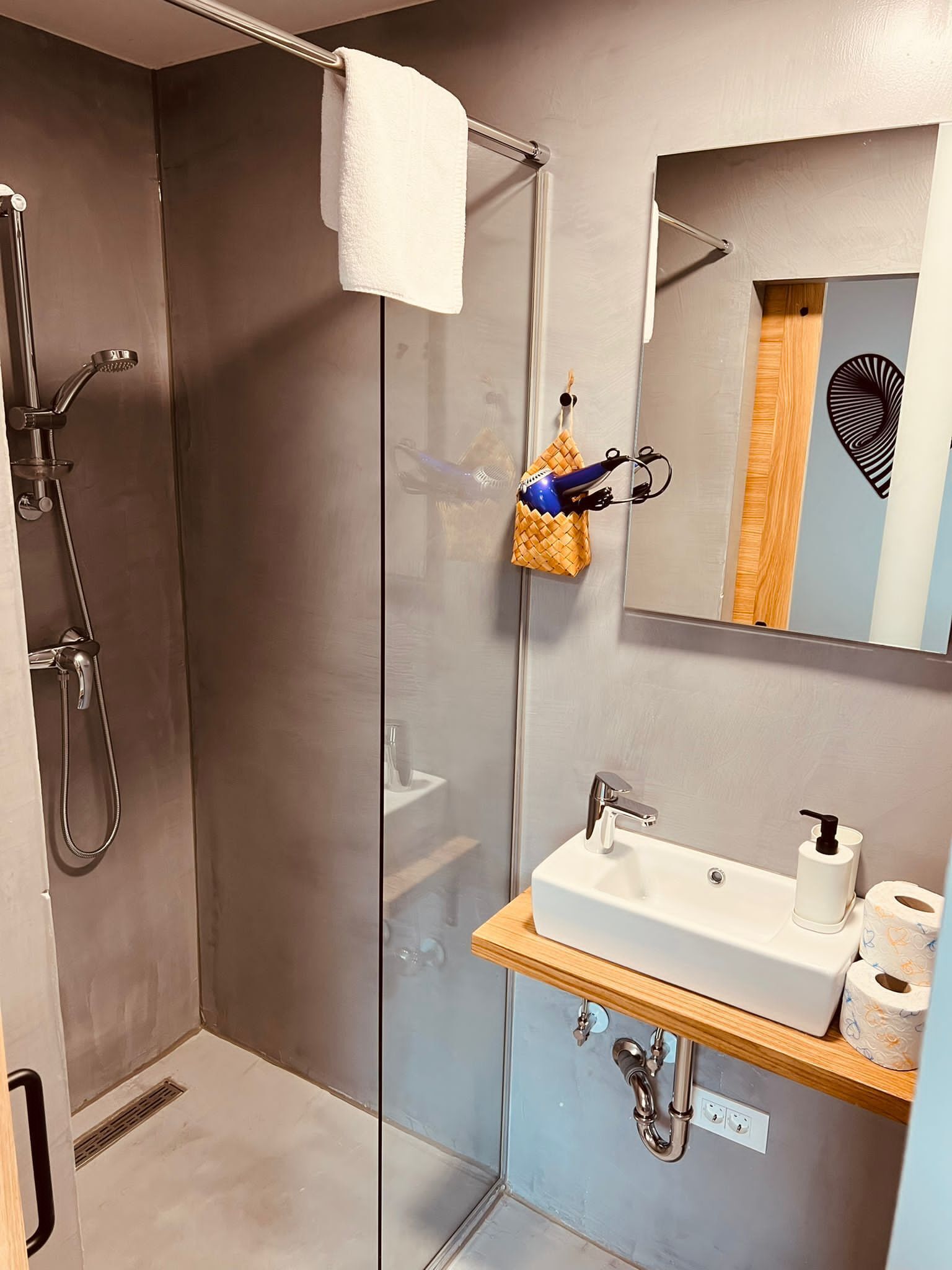 Un baño moderno con ducha de vidrio, lavabo blanco y espejo con un detalle decorativo en la pared.