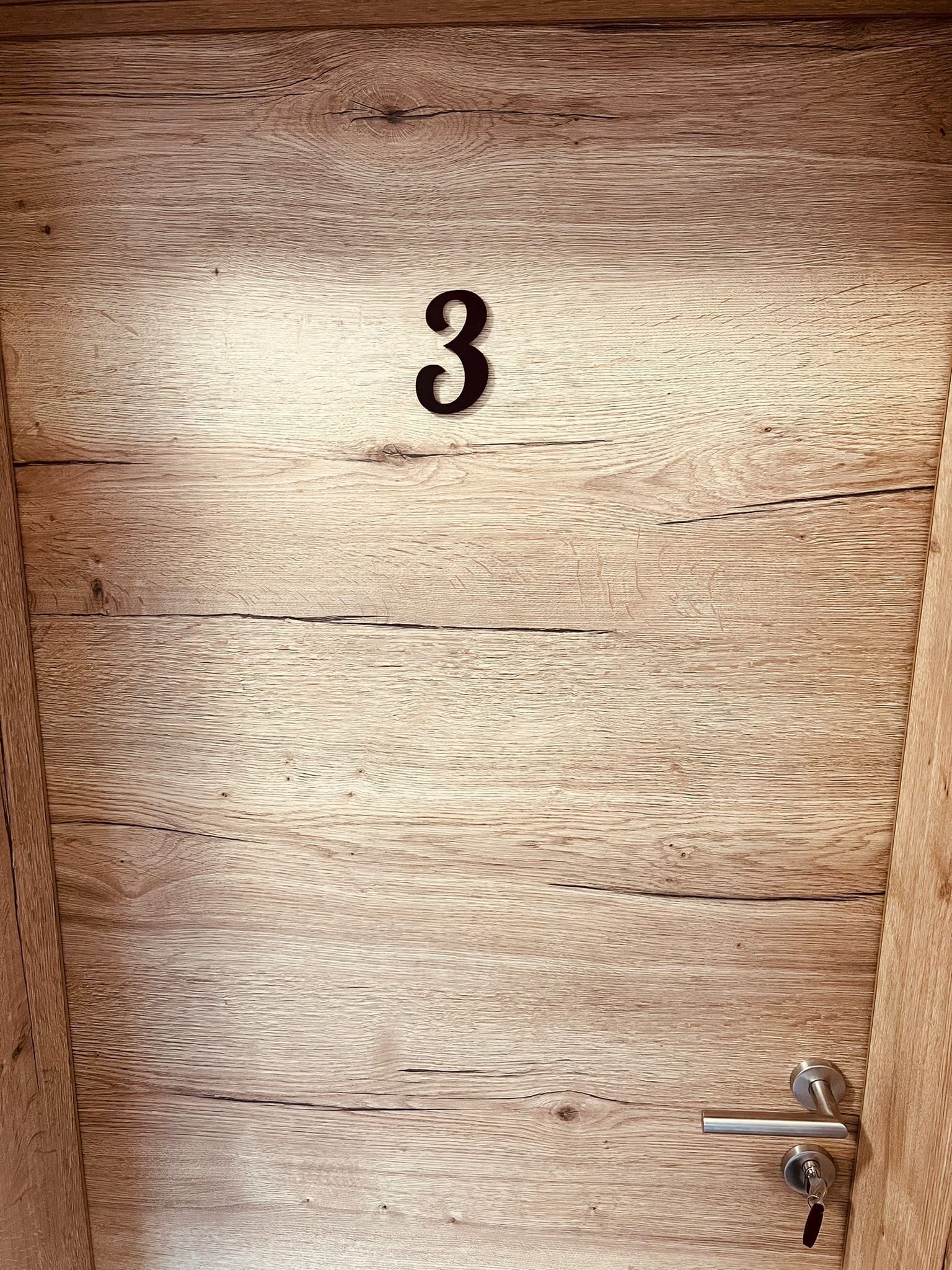Une porte en bois portant le numéro 3, une poignée de porte et un trou de serrure.