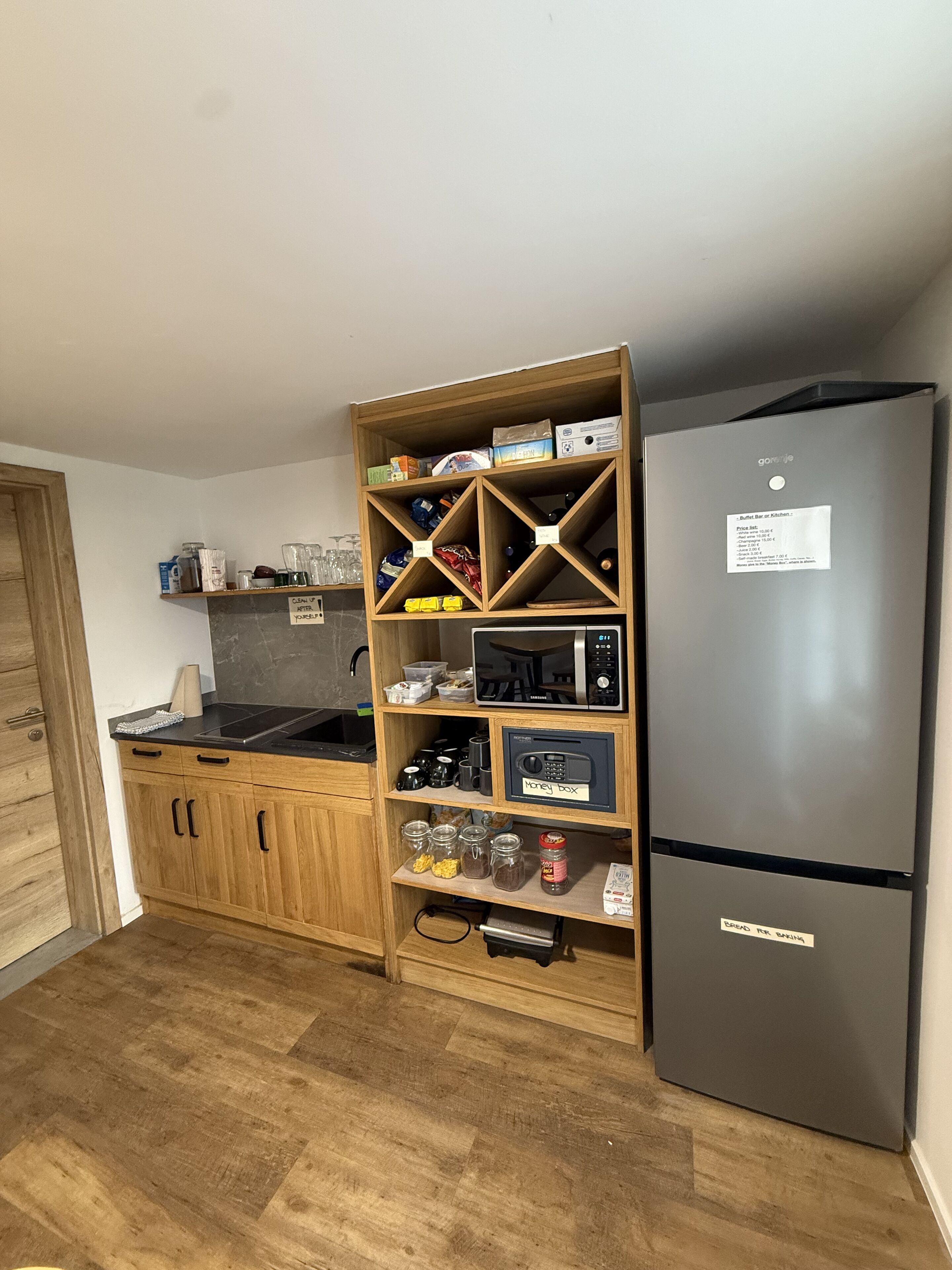 Una cocina con armarios de madera, una encimera negra, un refrigerador de acero inoxidable y una alacena empotrada con diversos utensilios de cocina.