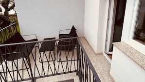 A balcony with a table and chairs, a window, and a door.