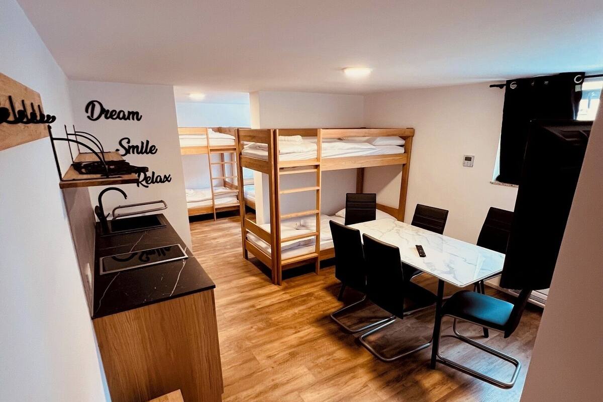 A modern room with bunk beds, a dining table with chairs, a small kitchen area, and a wall with motivational words.