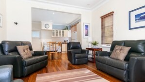 A modern living room with leather sofas, a wooden dining table, and a kitchen in the background.