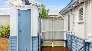 A portable toilet with a sign reading "CONFESSIONAL" and a bench outside.