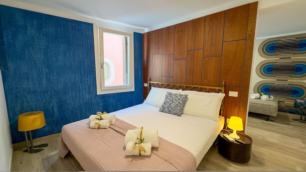 A hotel room with a bed, a window, a bedside table with a lamp, and a wall with a geometric pattern. - Ca de la Corona - Ipnosi by Ca-sa Check (Chioggia)