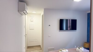 A modern hotel room with a flat-screen TV mounted on the wall, a wooden floor, and a door leading to another room. - Ca de la Corona - Ipnosi by Ca-sa Check (Chioggia)