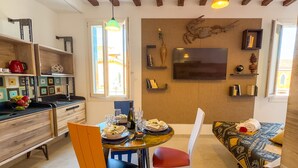 Un coin repas accueillant avec une table dressée pour deux personnes, un canapé et un téléviseur fixé au mur.