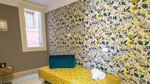 A room with a yellow patterned sofa, a blue cushion, and a floral wallpaper.