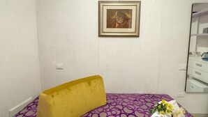 A hotel room with a bed, a framed painting, a mirror, and a small table with towels and flowers.