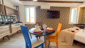 Une chambre d’hôtel compacte comprenant un coin repas, un lit avec des serviettes et une rose, ainsi qu’un téléviseur fixé au mur.