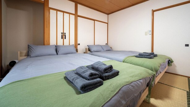 A hotel room with two beds, each with a green blanket and grey towels. - Lilac (Sapporo)
