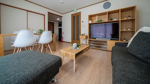 A modern living room with a sofa, a TV, a wooden coffee table, and a dining area with chairs. - Lilac (Sapporo)