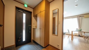 A hotel room with a wooden wardrobe, a small table with chairs, and a window with curtains. - Lilac (Sapporo)