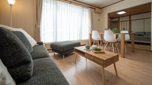 A modern living room with a sofa, ottoman, and a dining area with chairs and a table. - Lilac (Sapporo)