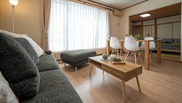 A modern living room with a sofa, ottoman, and a dining area with chairs and a table. - Lilac (Sapporo)