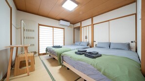 A traditional Japanese-style room with tatami flooring, two beds with green and blue bedding, a wooden desk, and a sliding door. - Lilac (Sapporo)