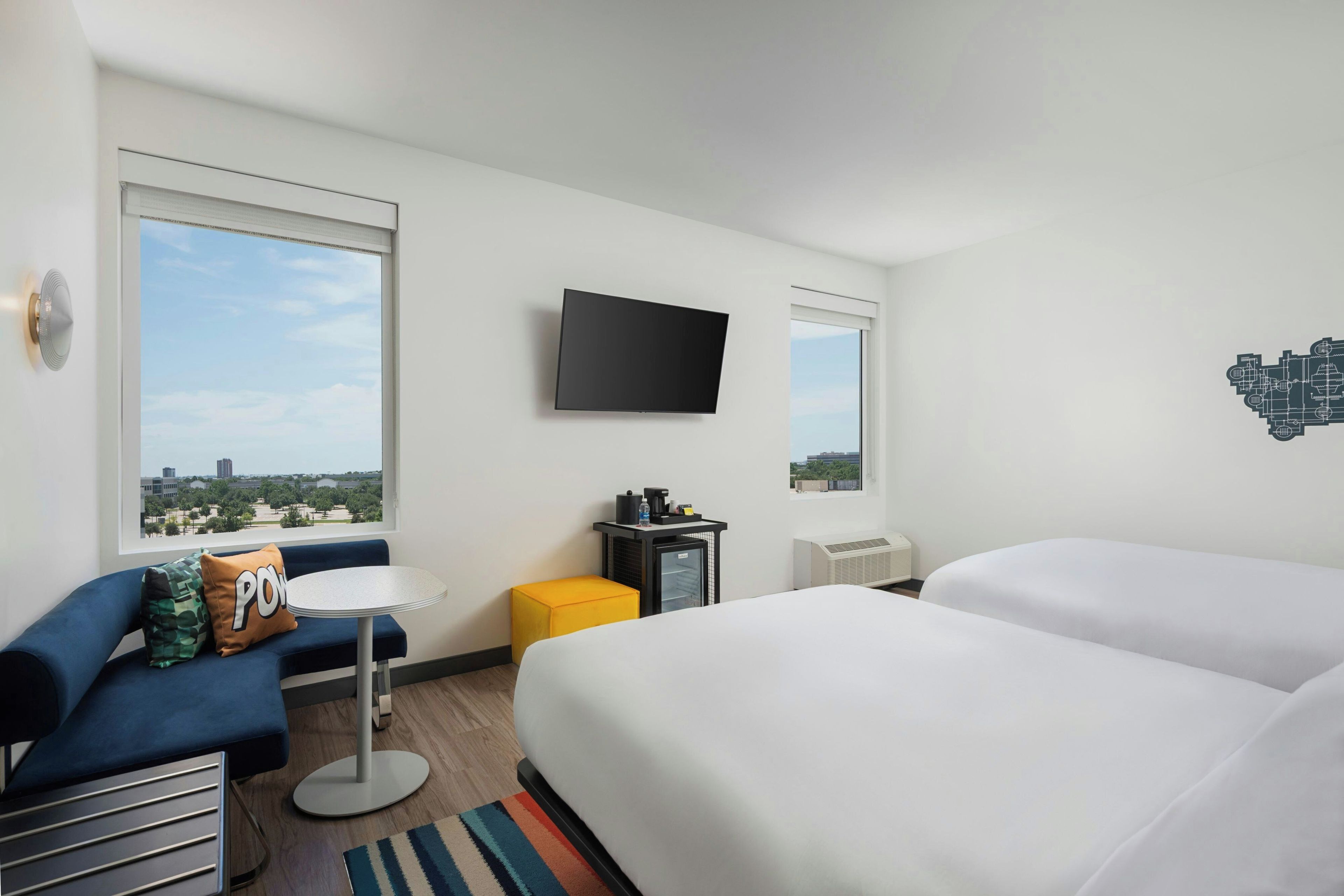 Una camera d'albergo con un letto, un divano, un tavolino, una TV e una finestra vista città.