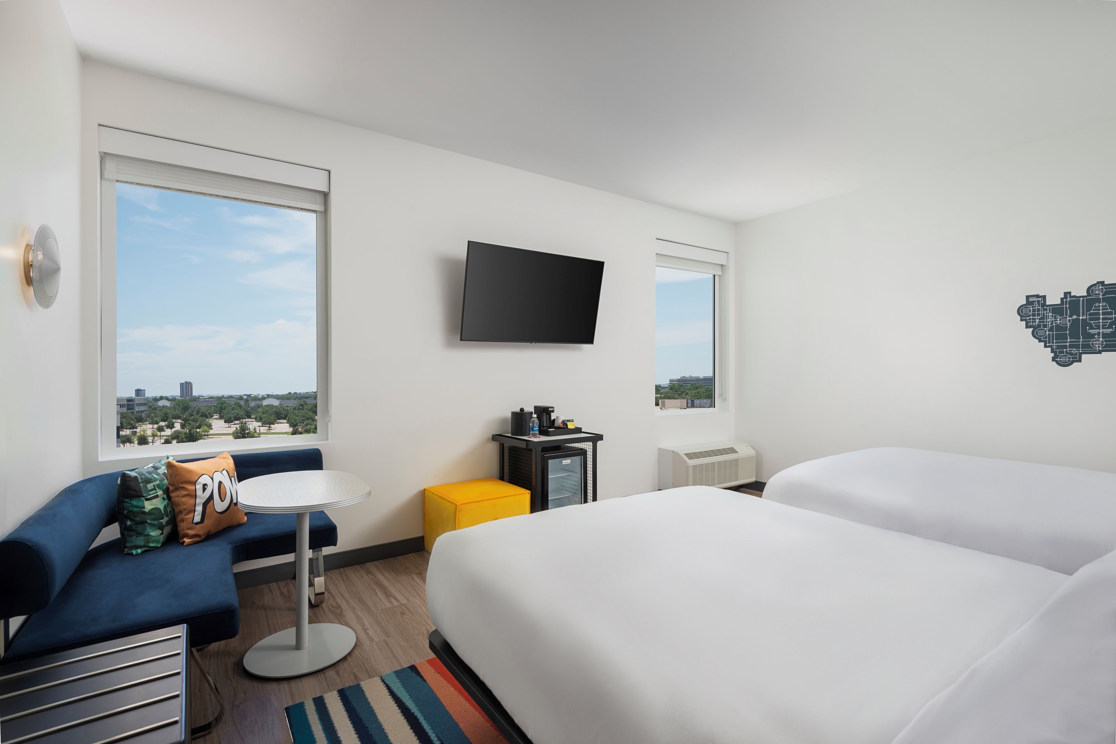A hotel room with a bed, a sofa, a small table, a TV, and a window with a city view.