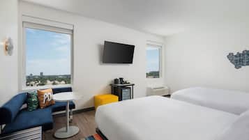 A hotel room with a bed, a sofa, a small table, a TV, and a window with a city view.
