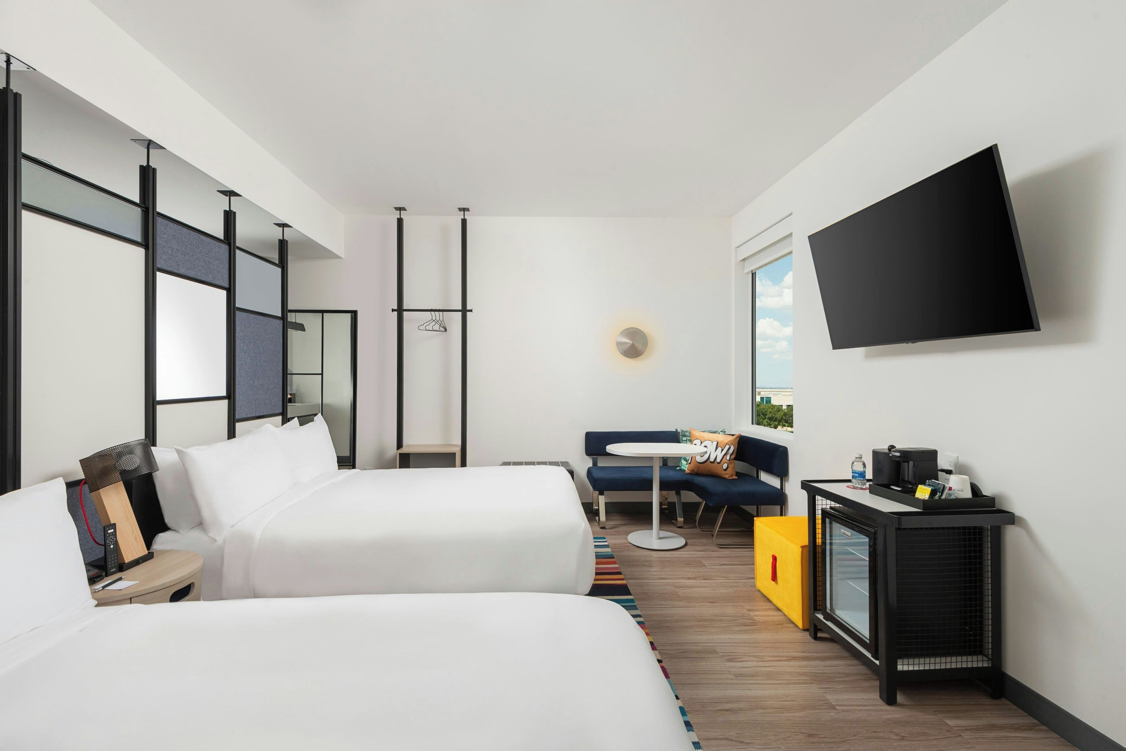 Una habitación de hotel moderna con cama, escritorio, silla, televisor y ventana.