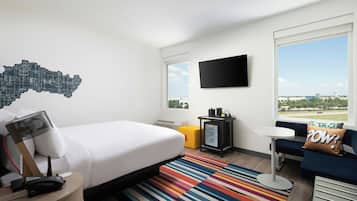 A hotel room with a bed, a desk, a chair, a TV, and a window with a cityscape view.