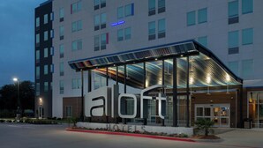 Un hotel moderno con un cartello 'aloft' ben visibile, ampie finestre e un'area d'ingresso coperta.