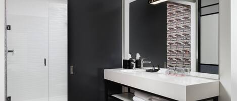 A modern bathroom with a white vanity, black shelving, and a large mirror.