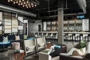 Un área de bar moderna con un letrero de neón, taburetes y un espacio de estar con sofás y sillas.