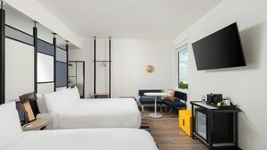 Una moderna camera d'albergo con due letti, un tavolino, una poltrona e una televisione, oltre a una finestra.