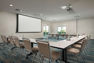 Un salón de conferencias con una pantalla grande, varias mesas y sillas.