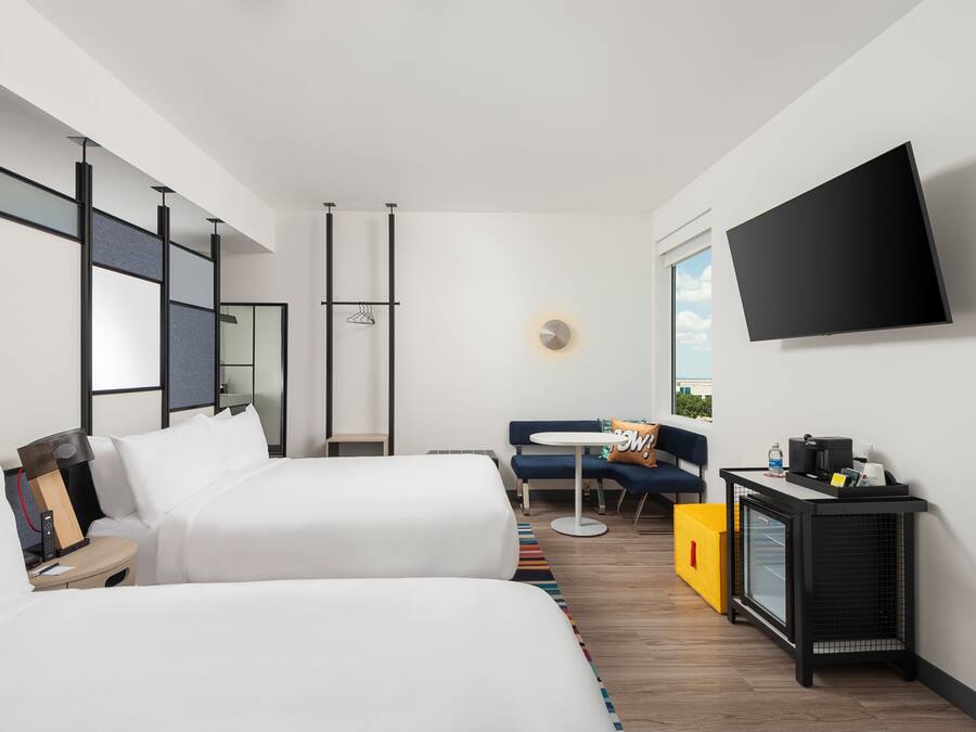 A modern hotel room with two beds, a flat-screen TV, a small table, and a sofa.